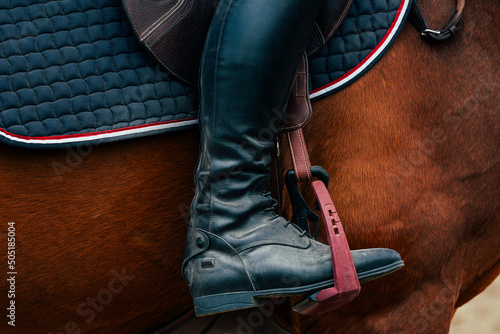 In the stirrup is the foot of a rider in a black boot. Equestrian sports. Horse riding.