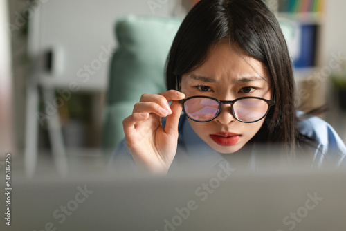 Confused Asian lady using laptop looking at screen photo