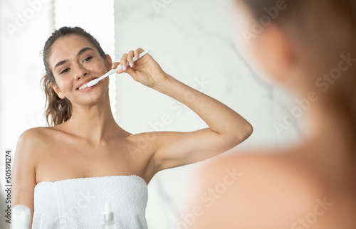 Happy Woman Brushing Teeth Caring For Oral Hygiene In Bathroom