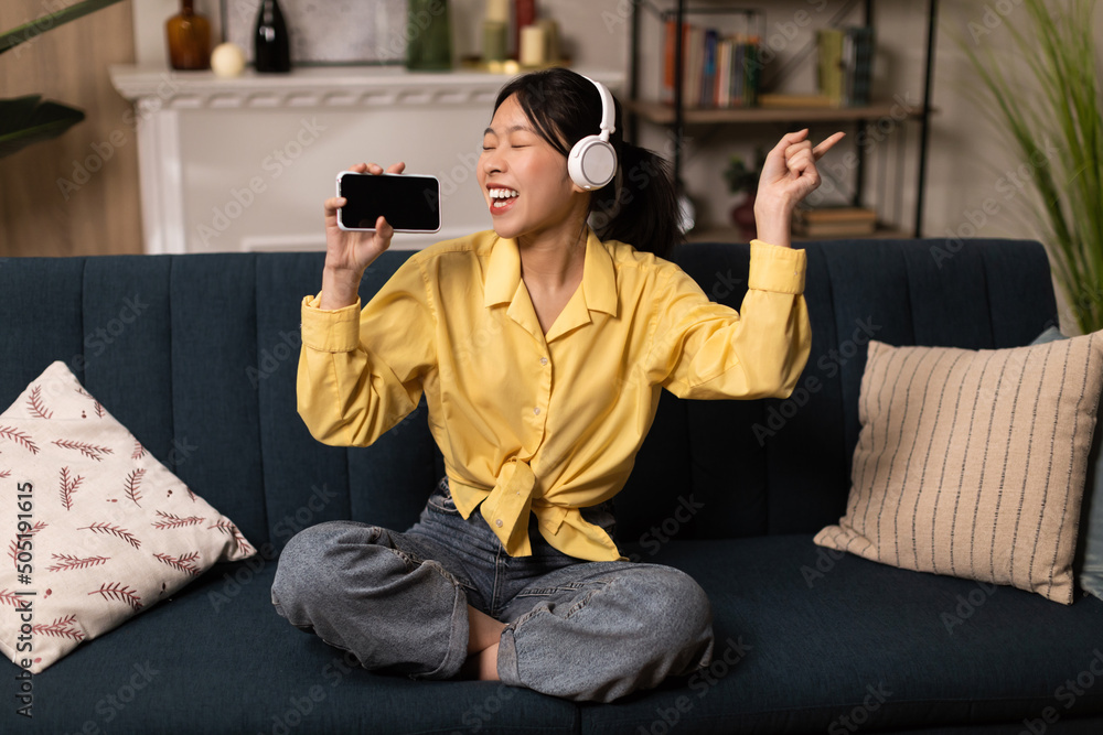 Obraz premium Excited Asian lady listening to music in headphones and dancing
