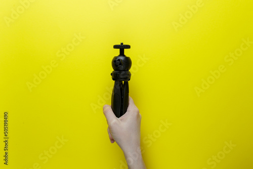 a girl holds a tripod in her hand next to a yellow background. blogger tool