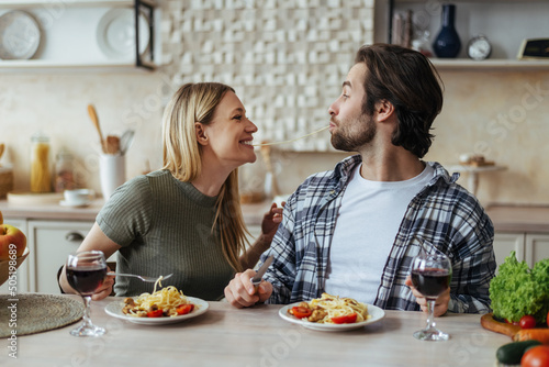 Glad happy handsome caucasian millennial couple eat pasta together  have fun in light kitchen interior  profile