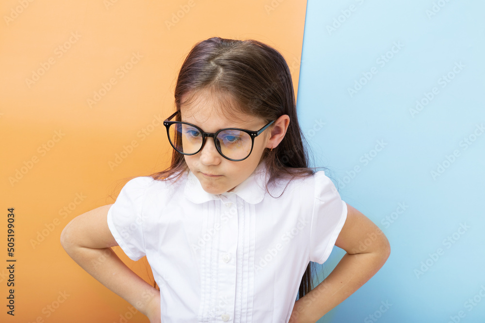 A 7-year-old girl with glasses with an angry face and hands on her sides. Children's education, learning concept