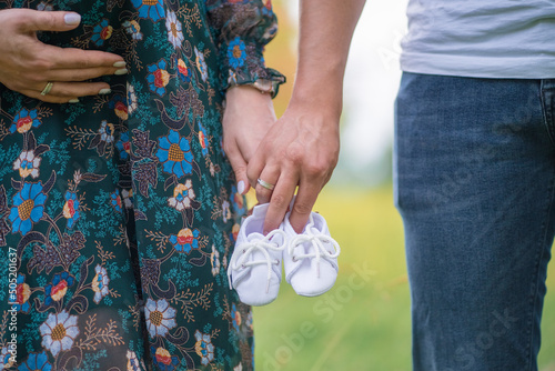 pregnant woman and man holding hands and holding baby shoes outdoors. pregnancy