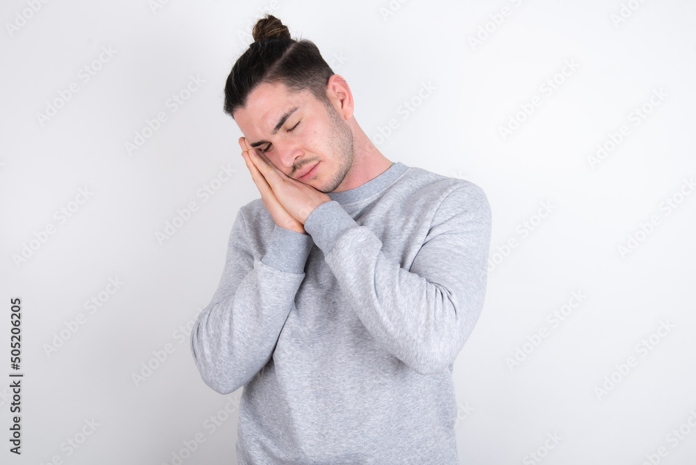 Young handsome dark haired man wearing fitted T-shirt over white wall sleeping tired dreaming and posing with hands together while smiling with closed eyes. Young handsome dark haired man wearing fitted T-shirt over white wall sleeping tired dreaming and posing with hands together while smiling with closed eyes.