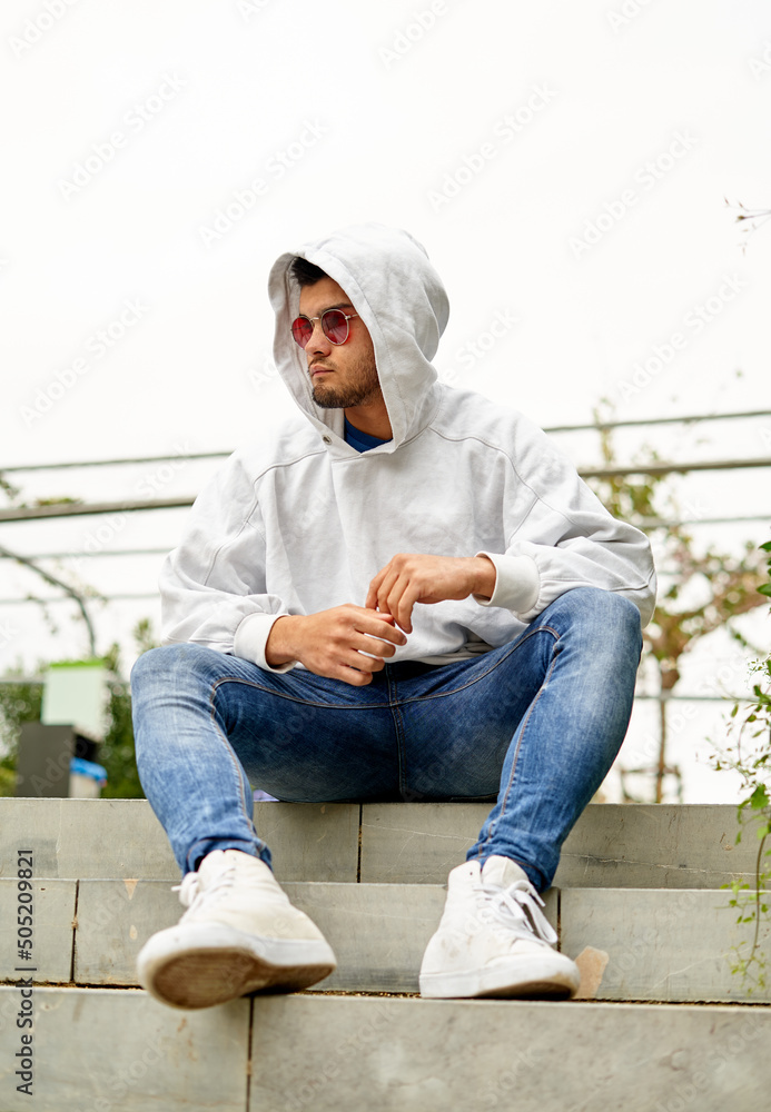 young man sitting with the hood of the sweatshirt and with red glasses young man sitting with the hood of the sweatshirt and with red glasses