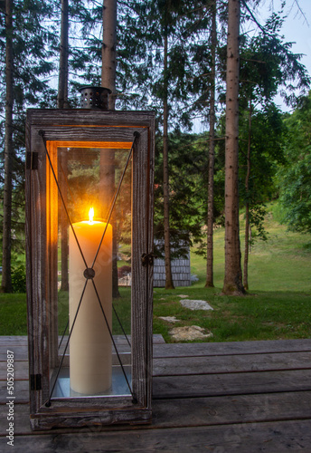 Outdoor lamp glowing in the forest. Home outdoor decor. Vertical photo. White candle.