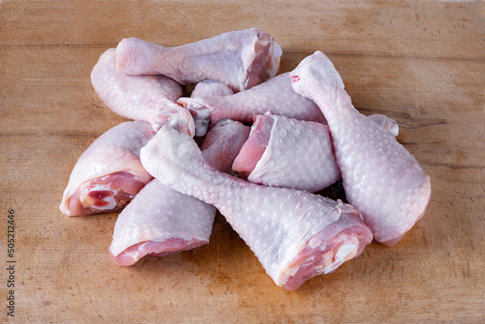 Close-up of several fresh uncooked chicken drumsticks laid out in a heap on a wooden cutting board. Selective focus.