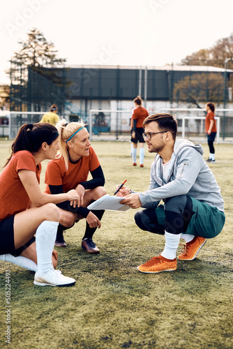 Young coach and female soccer players analyzing game plan on playing field.