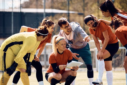 Young coach giving instructions to his female soccer team on playing field.