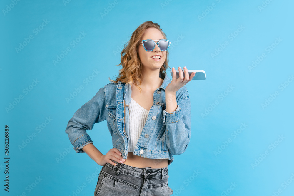 Young beautiful girl in casual style outfit using phone isolated on blue background. Concept of beauty, art, fashion, youth, fall collection Young beautiful girl in casual style outfit using phone isolated on blue background. Concept of beauty, art, fashion, youth, fall collection
