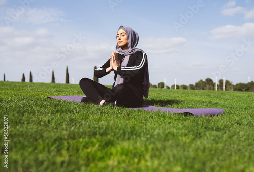Canvas Print muslim woman doing yoga on the mat in the park, healthy life concept