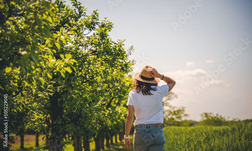Young woman in a white t-shirt hat and jeans walking in the summer garden © olezzo