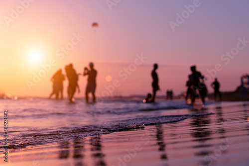 Silhouettes of blurry people on the seashore during sunset in summer in Antalya. Focus on foreground. Ripples and reflections on water surface. Tropical summer holiday.  photo