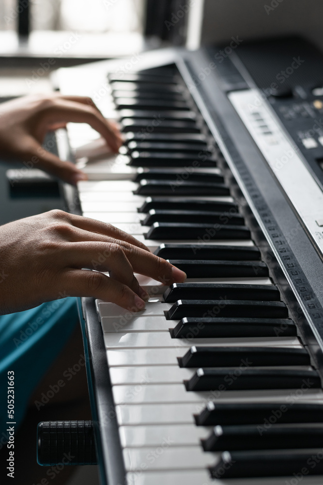 Fototapeta premium detailed view of the hands of a young latin man composing melodies on his electronic piano or synthesizer. boy practicing his virtual lessons from home. brown man practicing his hobby.