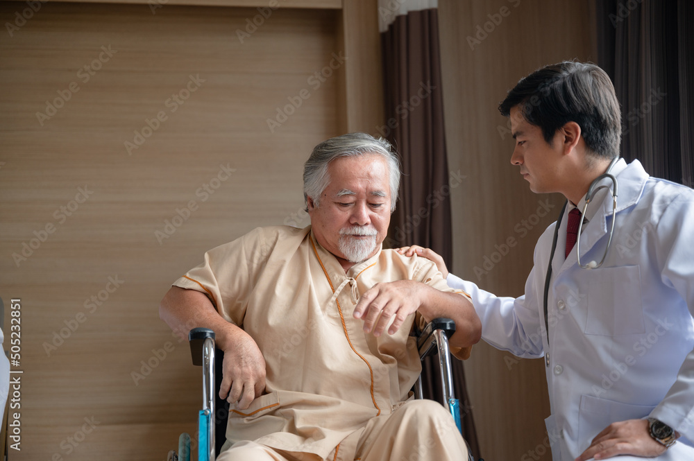 Fototapeta premium Senior male patient sitting on wheelchair in hospital smiling and talking and showing something outside the window to handsome doctor in labcoat