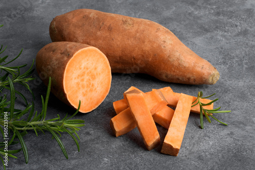 Raw whole orange sweet potato and slices of batatas with fresh rosemary on grey concrete background, close up photo