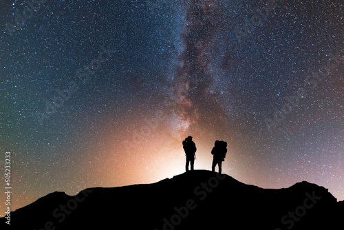 Silhouette of two traveler on the hill in starry night sky. Bright milky way galaxy behind him. 