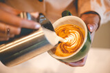 Closeup of hands of a male barista creating pattern and design using cream and utensil on freshly brewed and made cappacino coffee and frappe in cafeteria for customer