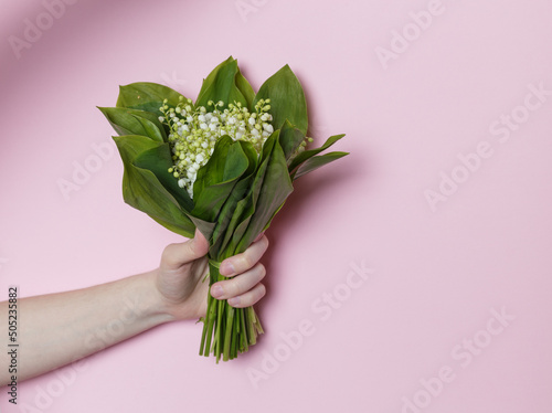 girl holding a bouquet of lilies of the valley in her hand on a pink background