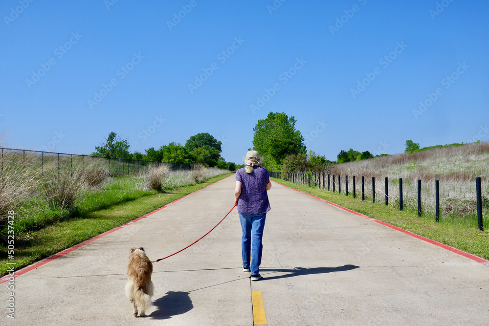A woman walking her dog along a trail in the Great Trinity Forest, an expansive urban park within Dallas, Texas. A woman walking her dog along a trail in the Great Trinity Forest, an expansive urban park within Dallas, Texas.