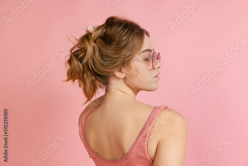 Monochrome portrait of young attractive woman in crop top isolated on pink background. Concept of beauty, art, fashion, youth. Back view