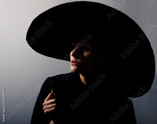 Glamorous woman in a big black hat and coat play of light and shadow