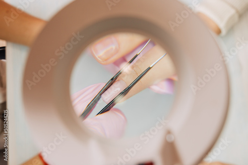 Manicure process. The master forms an artificial nail from a special gel using tweezers. View through a lamp with a magnifying glass.