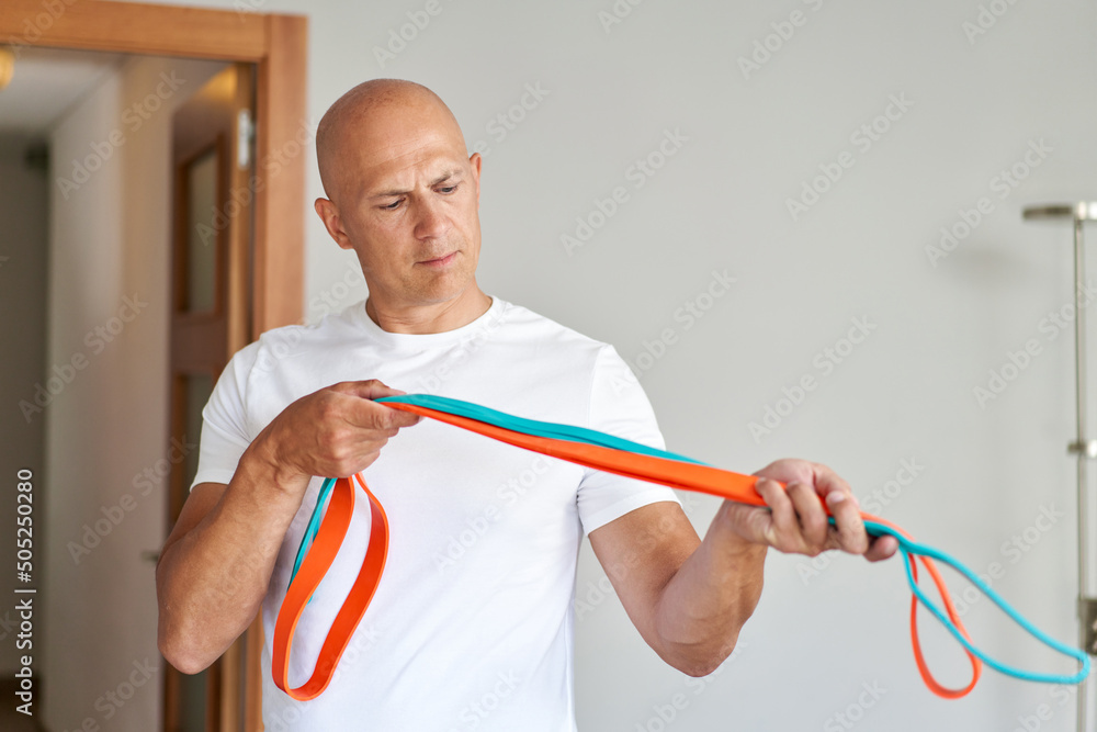 Handsome sports man doing shoulder lateral raise exercise with resistance band at home Handsome sports man doing shoulder lateral raise exercise with resistance band at home