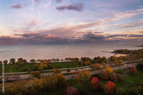 A beautiful autumn sunset over Lake Michigan and Lake Shore Drive in Chicago with pink and blue clouds and red, yellow and green fall foliage.