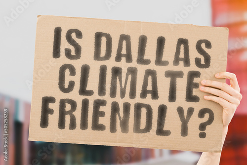 The question " Is Dallas climate-friendly? " is on a banner in men's hands with blurred background. Support. Team. Activist. Urban. Sunset. Carbon. Ecology. Energy. New. Clean. Warming. Waste © AndriiKoval