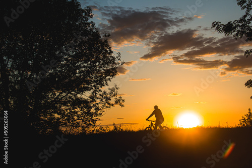 A cyclist rides through a field against the backdrop of a beautiful contour sunset light. Beautiful sunset. Photo of nature. Velotheme.