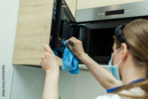 Woman cleaning oven and microwave with rag in kitchen
