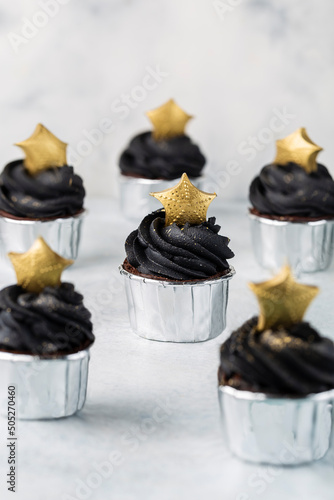 Black cupcakes decorated with a gold staron a light background photo