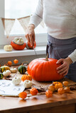 Woman carves a pumpkin for handmade Jack-O-lantern at home for Halloween party decoration. Concept of holiday seasonal handmade decor. Autumn colors, faceless, close-up