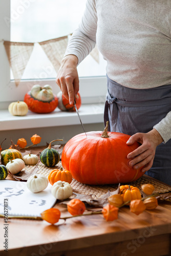 Woman carves a pumpkin for handmade Jack-O-lantern at home for Halloween party decoration. Concept of holiday seasonal handmade decor. Autumn colors, faceless, close-up