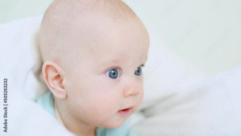 beautiful blue eyed infant baby portrait close-up, smiling face of little child lying in white bed on stomach. happy caucasian toddler baby portrait, funny kid looking camera opening mouth, emotions beautiful blue eyed infant baby portrait close-up, smiling face of little child lying in white bed on stomach. happy caucasian toddler baby portrait, funny kid looking camera opening mouth, emotions