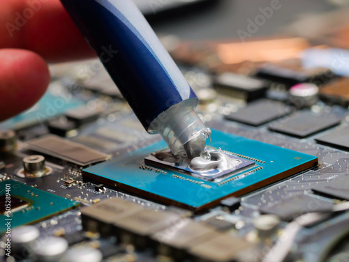 The close up image of technician squeezing the fresh thermal paste compound on the top of GPU in the socket. The concept of laptop hardware, repairing, upgrade and technology.