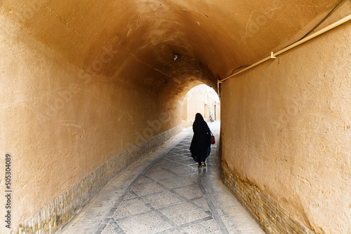 Fotografia Iranian woman wearing black chador walking along street of Yazd