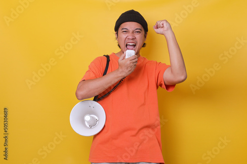 Asian young man in casual style giving spirit using megaphone isolated on yellow background. 
