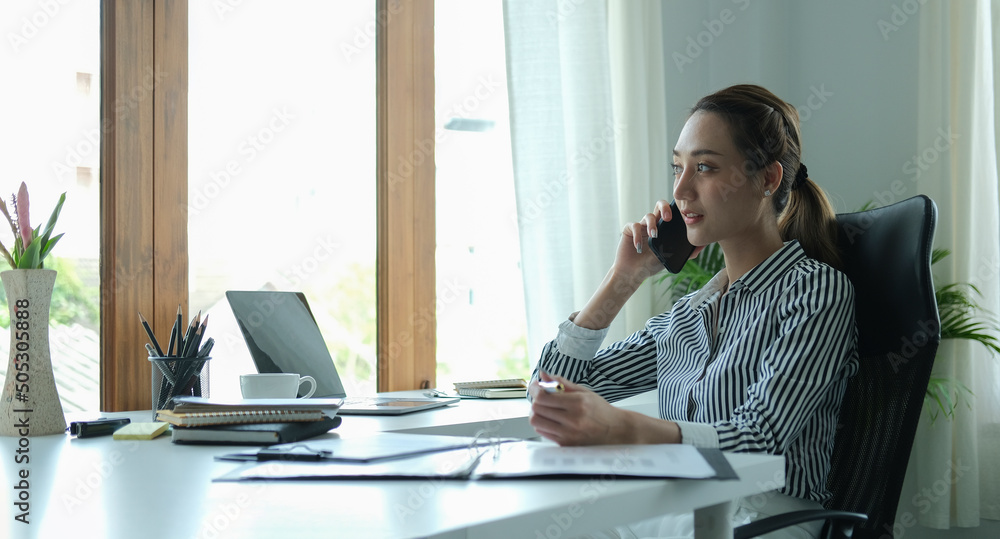 Smiling female entrepreneur sitting at bright modern office and talking on mobile phone. Smiling female entrepreneur sitting at bright modern office and talking on mobile phone.