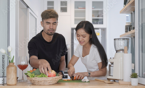 Happy couple standing in kitchen making fresh vegetable salad together. Healthy lifestyle, Healthy food.