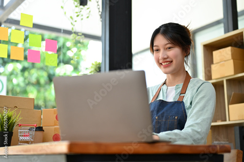 Female fashion shop owner using laptop computer to reply message from her customer