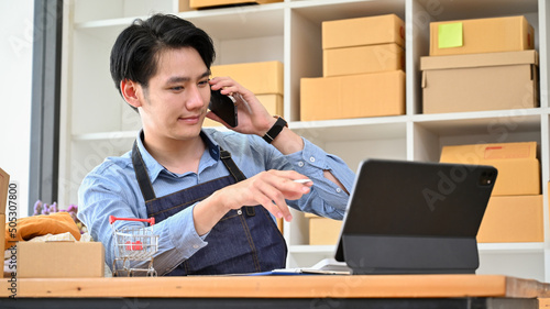 Male online business entrepreneur talking on the phone while looking some information on tablet screen.