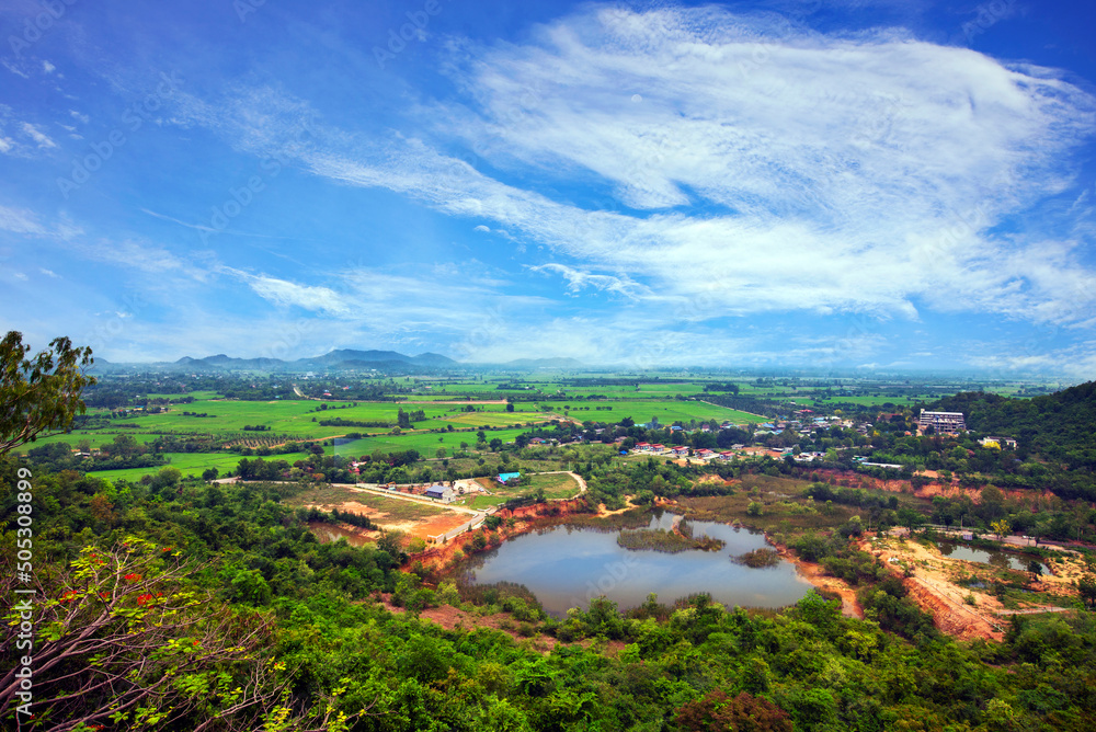 Obraz premium High angle view of fertile farming community in rural Thailand under bright blue sky and white clouds.
