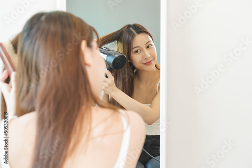 Hair Dryer, happy, asian young woman, girl looking into mirror reflect using hairdryer to dry, blowing long blonde straight after shower at home. Hairdressing, hair treatment and beauty health care.
