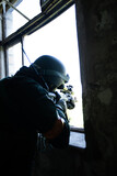 Ukrainian military sniper militant kissing from the window. a soldier in uniform and helmet holds a weapon leaning against the windowsill. rear view. medium plan