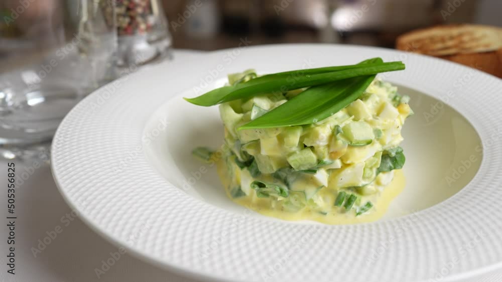 White plate with a salad of wild garlic, cucumber, boiled egg and sour cream rotates on the table in the kitchen, close up White plate with a salad of wild garlic, cucumber, boiled egg and sour cream rotates on the table in the kitchen, close up