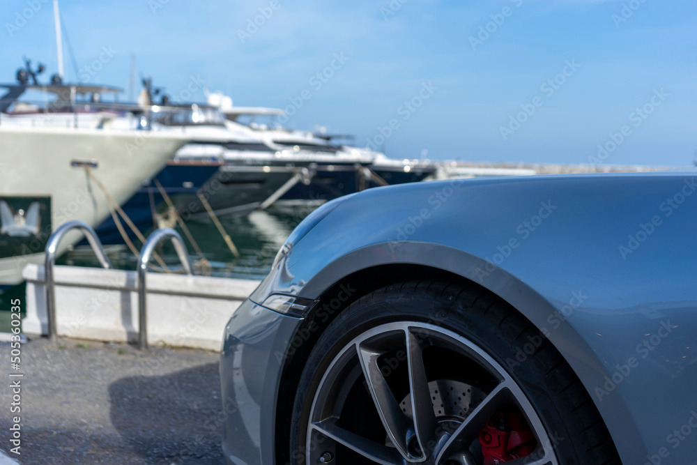 PANORAMIC VIEW OF A LUXURY CAR AND YACHTS IN THE BACKGROUND PANORAMIC VIEW OF A LUXURY CAR AND YACHTS IN THE BACKGROUND