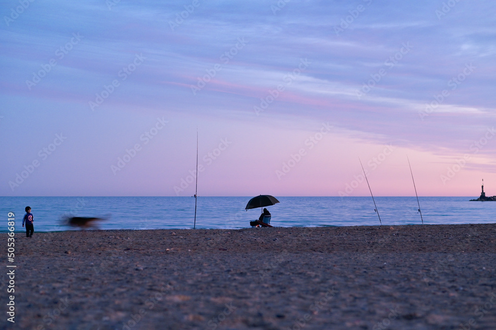 Horizontal tranquil scene at the beach during a blue Fall sunset with fishermen silhouette 